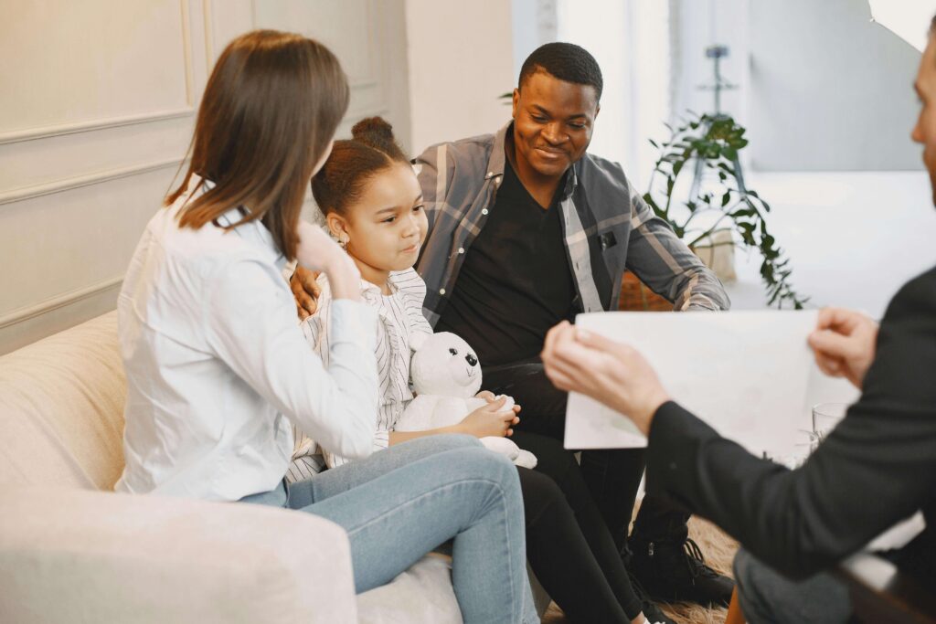 Parents sitting on couch with young daughter holding stuffed animal during consultation with professional showing paperwork. Get organized and know what to expect during the assessment with autism evaluations in Fort Collins, CO.