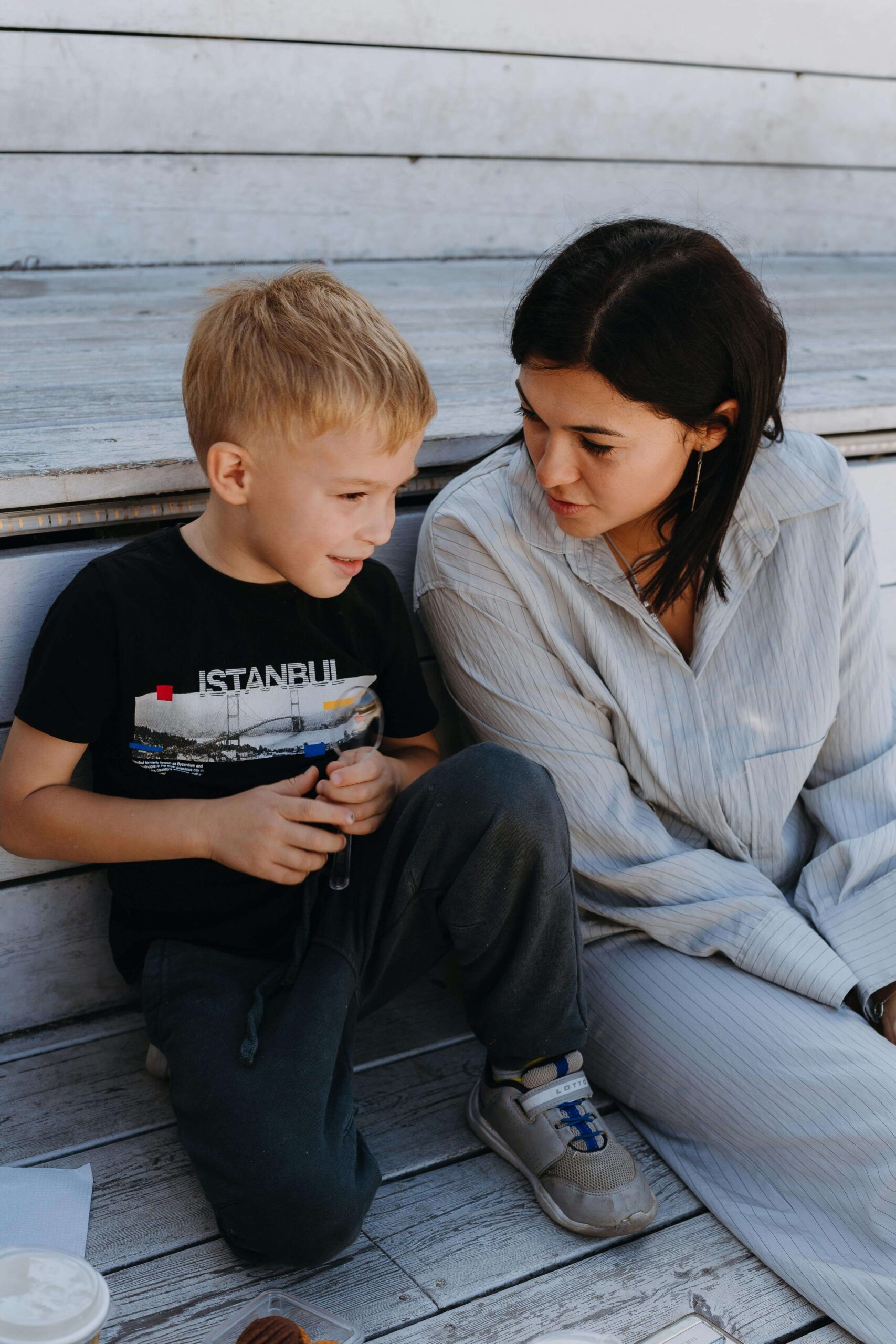Mother in striped shirt sitting on wooden deck having calm conversation with young son. Learn how to explain the evaluation process to your child with autism evaluations in Fort Collins, CO.