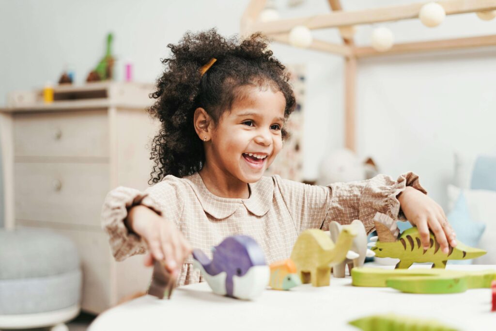 Happy little girl playing with dinosaur toys. With the support of ADHD testing in Fort Collins, CO your child can learn to manage their ADHD symptoms and begin thriving.