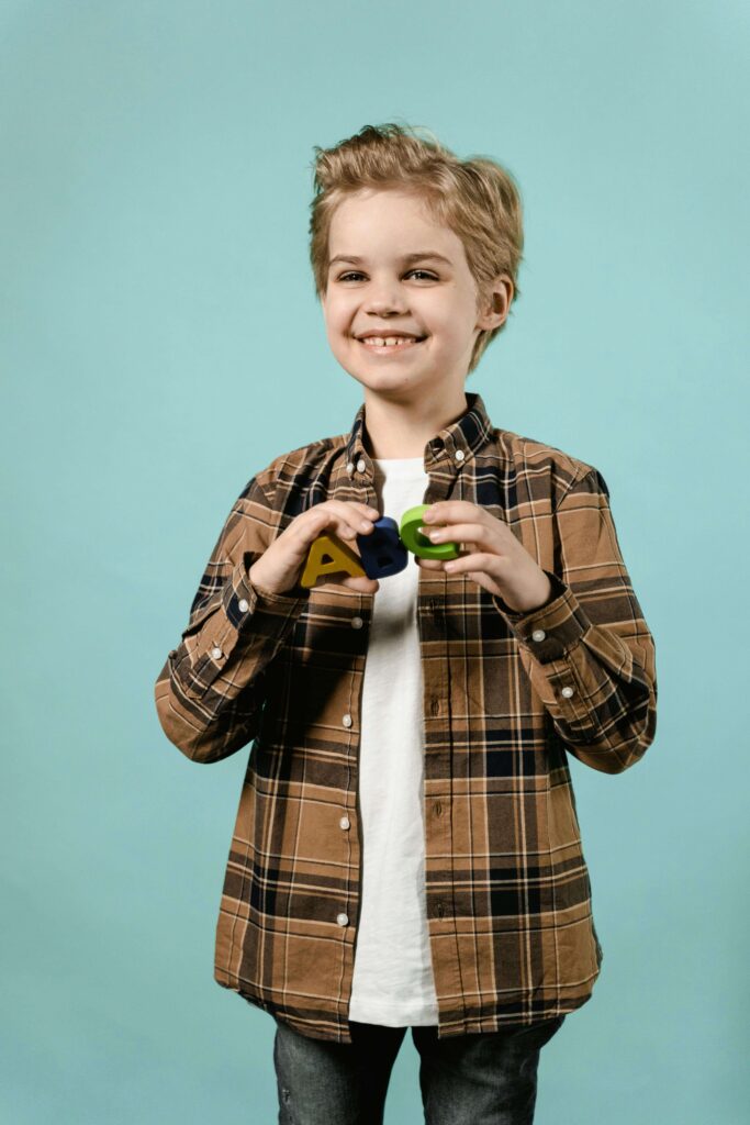 Smiling child in plaid shirt holding colorful ABC letters against turquoise background. Get clarity on your child's learning and attention challenges with expert ADHD testing for kids in Fort Collins, CO.