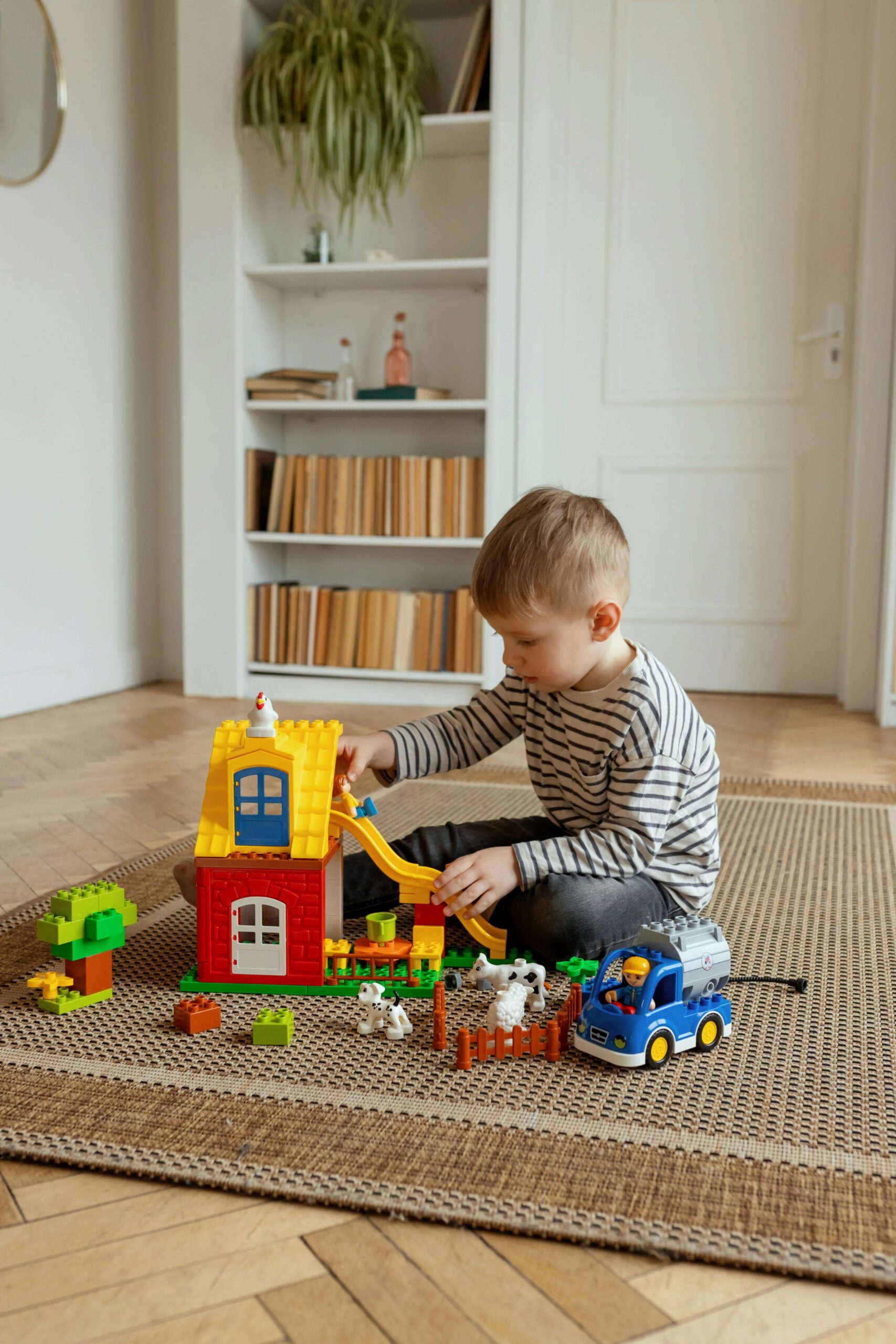 Young boy in striped shirt sitting on floor playing independently with colorful building blocks. Wondering if your child's behavior is typical or ADHD? Get clarity and answers with ADHD testing for kids in Fort Collins, CO.
